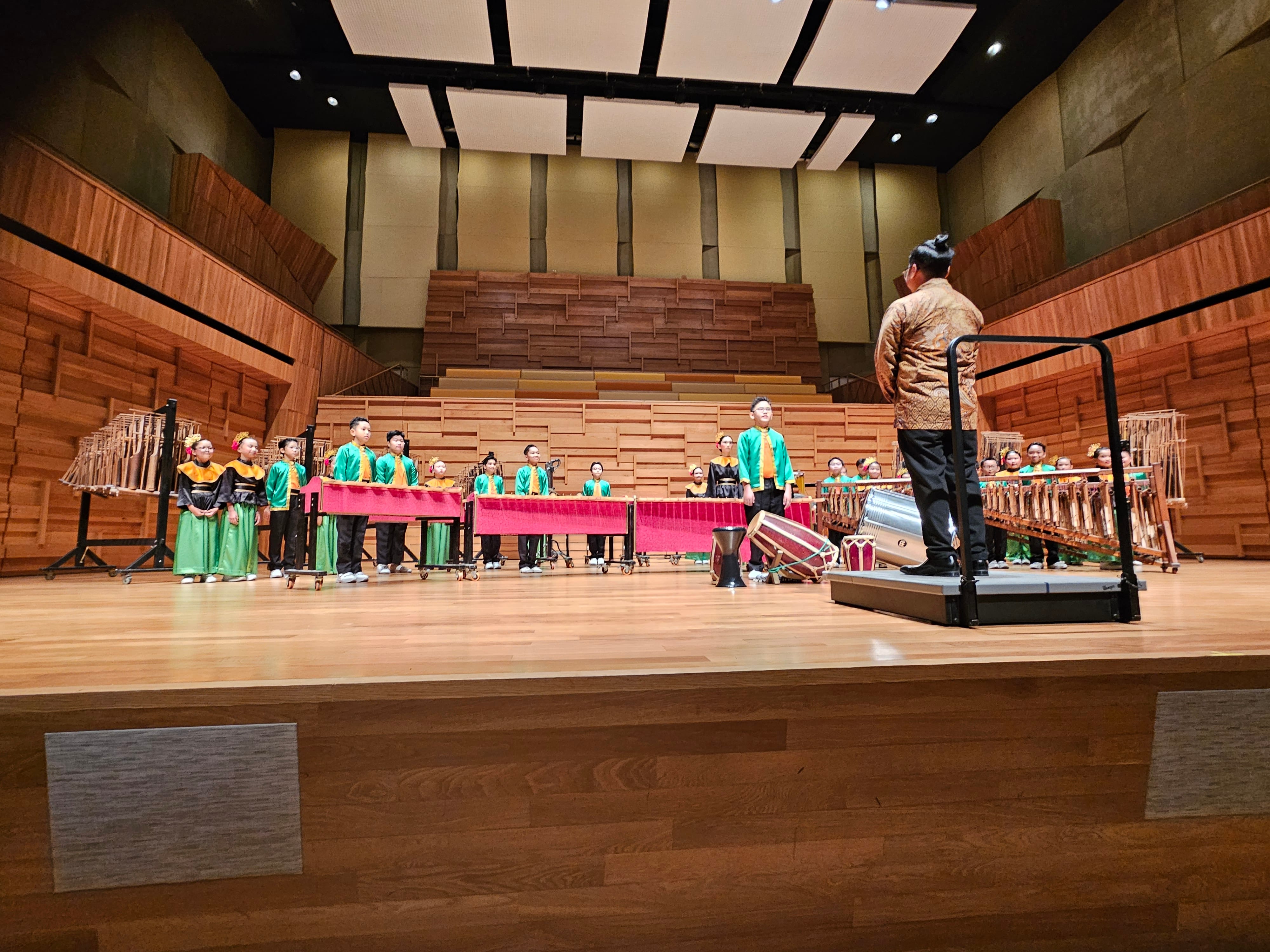 Children performing with Angklung instruments, facing their conductor